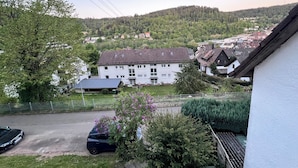 Et boligområde med en hvid bygning, en parkeret bil og en bakke i baggrunden.