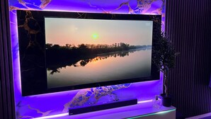 Et fladskærms-TV ophængt på en væg med et marmorlignende design, en plante og en hylde nedenunder.