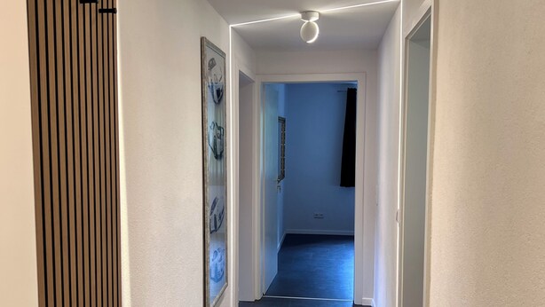 En gang med moderne design, mørkt flisegulv, hvide vægge og et loft med indbyggede spots.