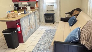 A compact living space with a kitchenette, a sofa, a patterned rug, and a small side table.