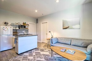 Une cuisine moderne équipée d’un réfrigérateur, d’un four à micro-ondes et d’un îlot central, ainsi qu’un canapé gris et une table basse avec des magazines.