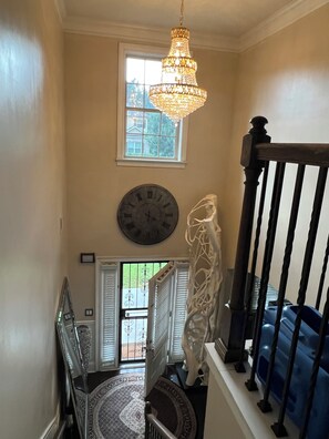 Eine Treppe mit einer Chandelier, einer Uhr und Blick durch ein Fenster.