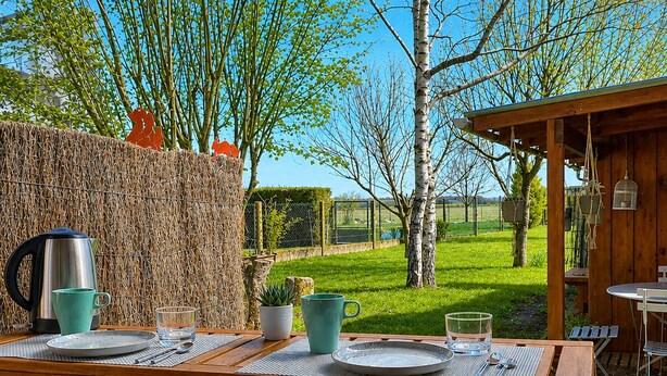 A wooden outdoor dining area with a table set for two, a kettle, and a potted plant. - Charming gîte de la Cour Suard (Cigogné)