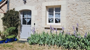 A stone building with a door and two windows, surrounded by plants and flowers. - Charming gîte de la Cour Suard (Cigogné)