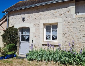 A stone building with a door and two windows, surrounded by plants and flowers. - Charming gîte de la Cour Suard (Cigogné)