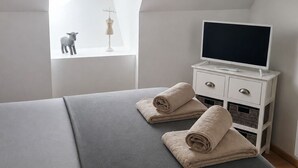 A bedroom with a bed, a TV on a white dresser, a skylight, and a small lamb figurine. - Charming gîte de la Cour Suard (Cigogné)