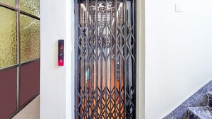 A metal gate with a fire exit sign above it, a digital elevator control panel, and a staircase with blue tiles. - Classic With Balcony Hotel SKR (Varanasi)