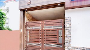 A double metal gate with horizontal bars and a central vertical divider, leading to a building with a stone-patterned roof and a white wall. - Classic With Balcony Hotel SKR (Varanasi)