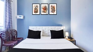 A hotel room with a white bed, black pillows, a blue wall, and three framed leaf artworks. - Classic With Balcony Hotel SKR (Varanasi)