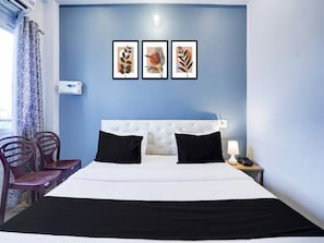 Ett hotellrum med en vit säng, svarta kuddar, en blå vägg och tre inramade konstverk med lövmotiv.