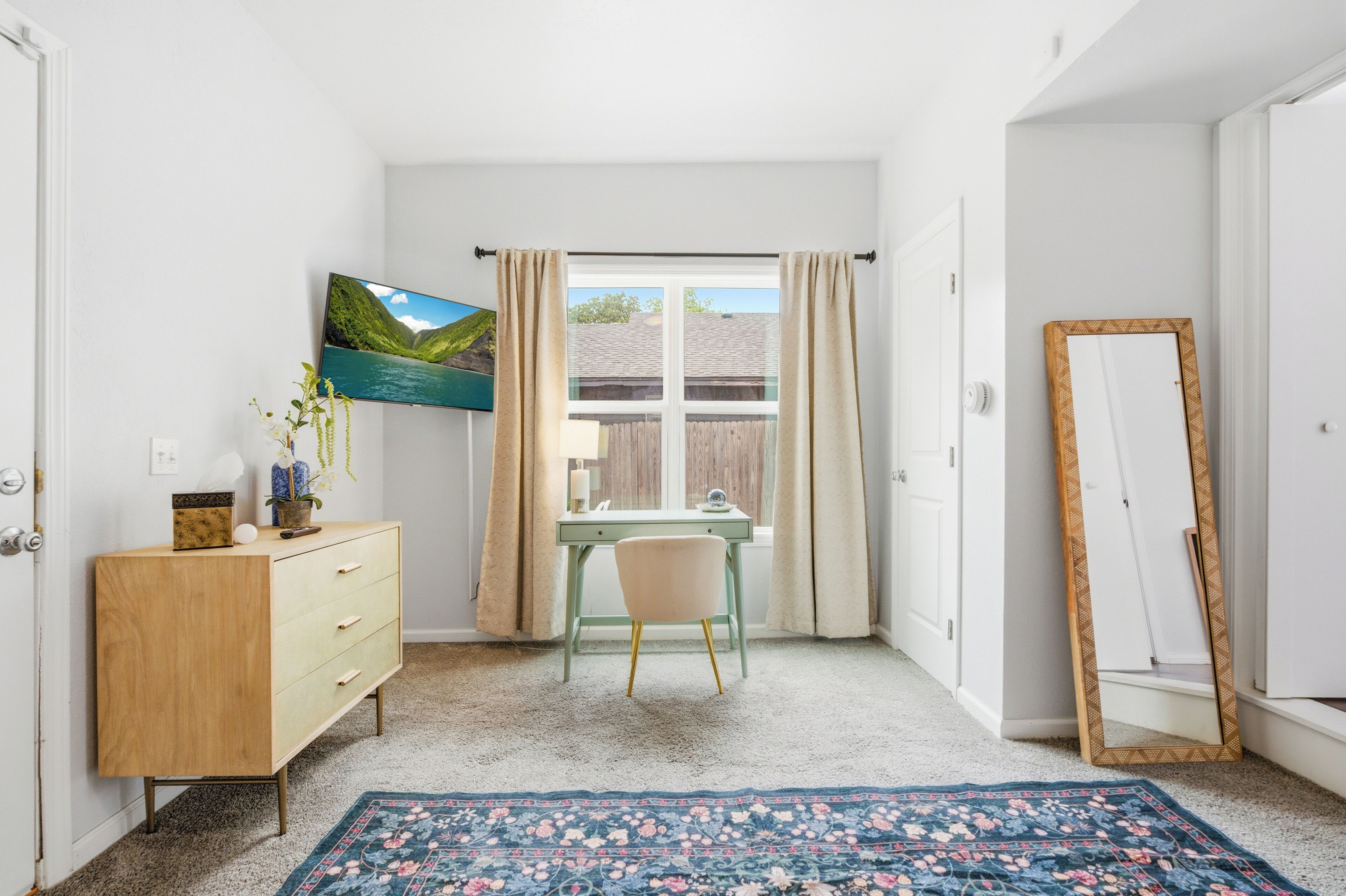 Una habitación con escritorio, silla, cómoda y un ventanal con cortinas.