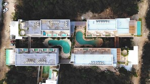 Vue aérienne d’un complexe hôtelier doté de plusieurs piscines, d’espaces de détente en plein air et d’un parking.