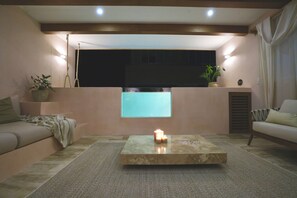 A modern living room with a sofa, a coffee table with candles, a potted plant, and a view through a window. - Tulum Jungle Oasis (Tulum)