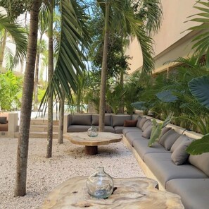A tropical outdoor seating area with a sofa and a round table, surrounded by palm trees and plants. - Tulum Jungle Oasis (Tulum)