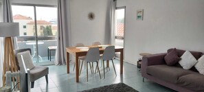 Ein modernes Wohnzimmer mit Essbereich, einer Couch und einem Balkon mit Blick auf Gebäude.