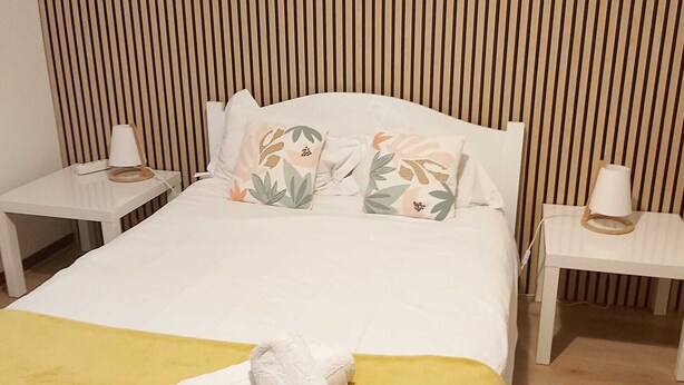 Un letto con testiera bianca, due comodini con lampade e una coperta gialla.