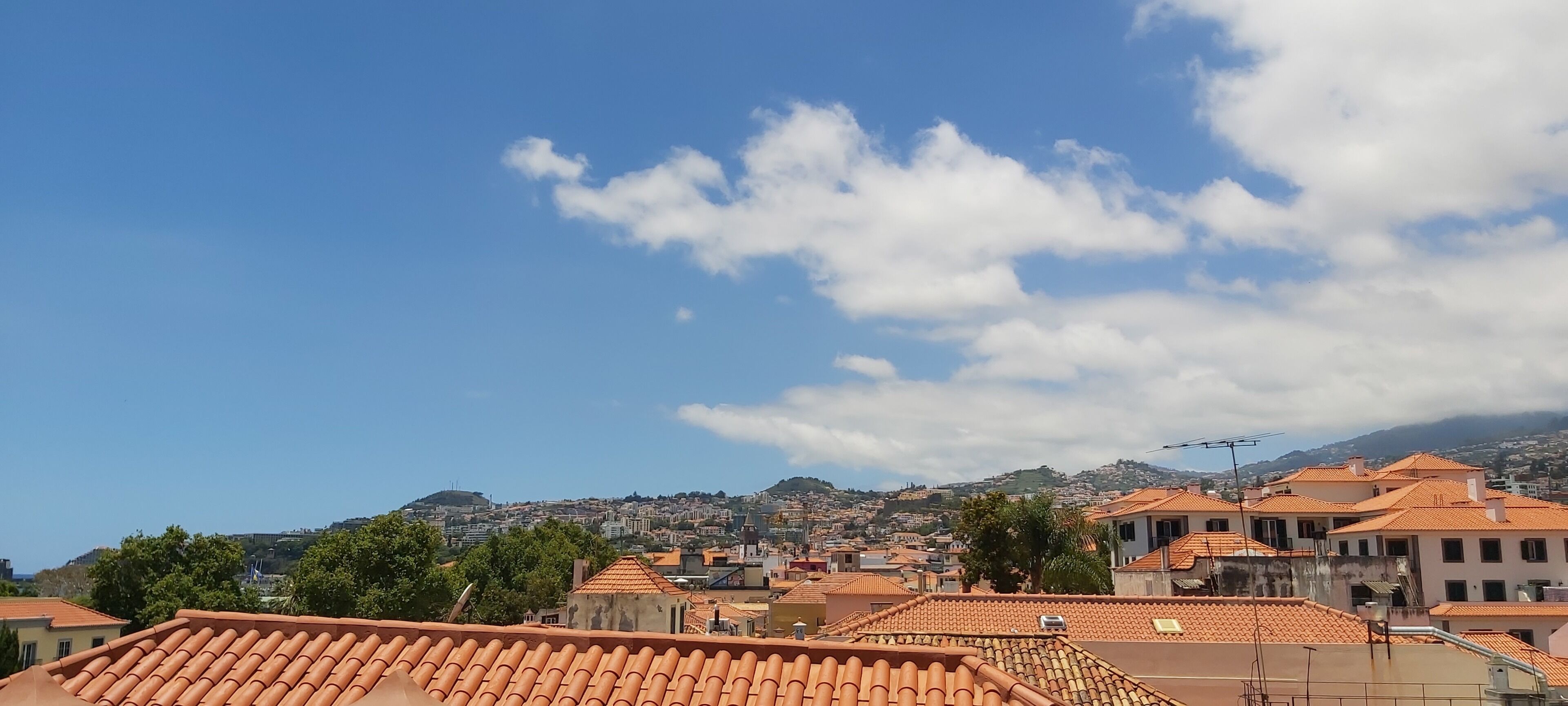 Une vue urbaine avec des bâtiments aux toits de tuiles rouges, un ciel dégagé et quelques nuages épars.