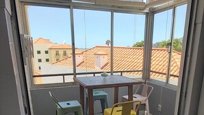 Una stanza con un tavolo e sedie, vista su edifici attraverso ampie finestre e pavimento piastrellato.