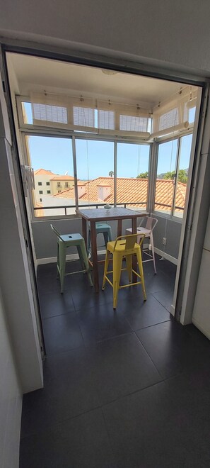 Ein Zimmer mit Tisch und Stühlen, Blick auf Gebäude durch große Fenster und ein gefliester Boden.