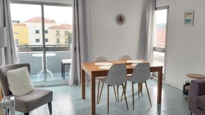 Un soggiorno moderno con un tavolo da pranzo, sedie, un divano e un balcone con vista sugli edifici.