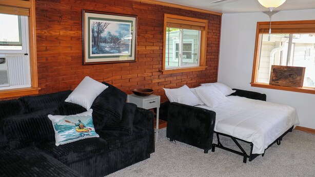 Um quarto com uma cama, um sofá preto, uma mesa de cabeceira branca e um quadro na parede.