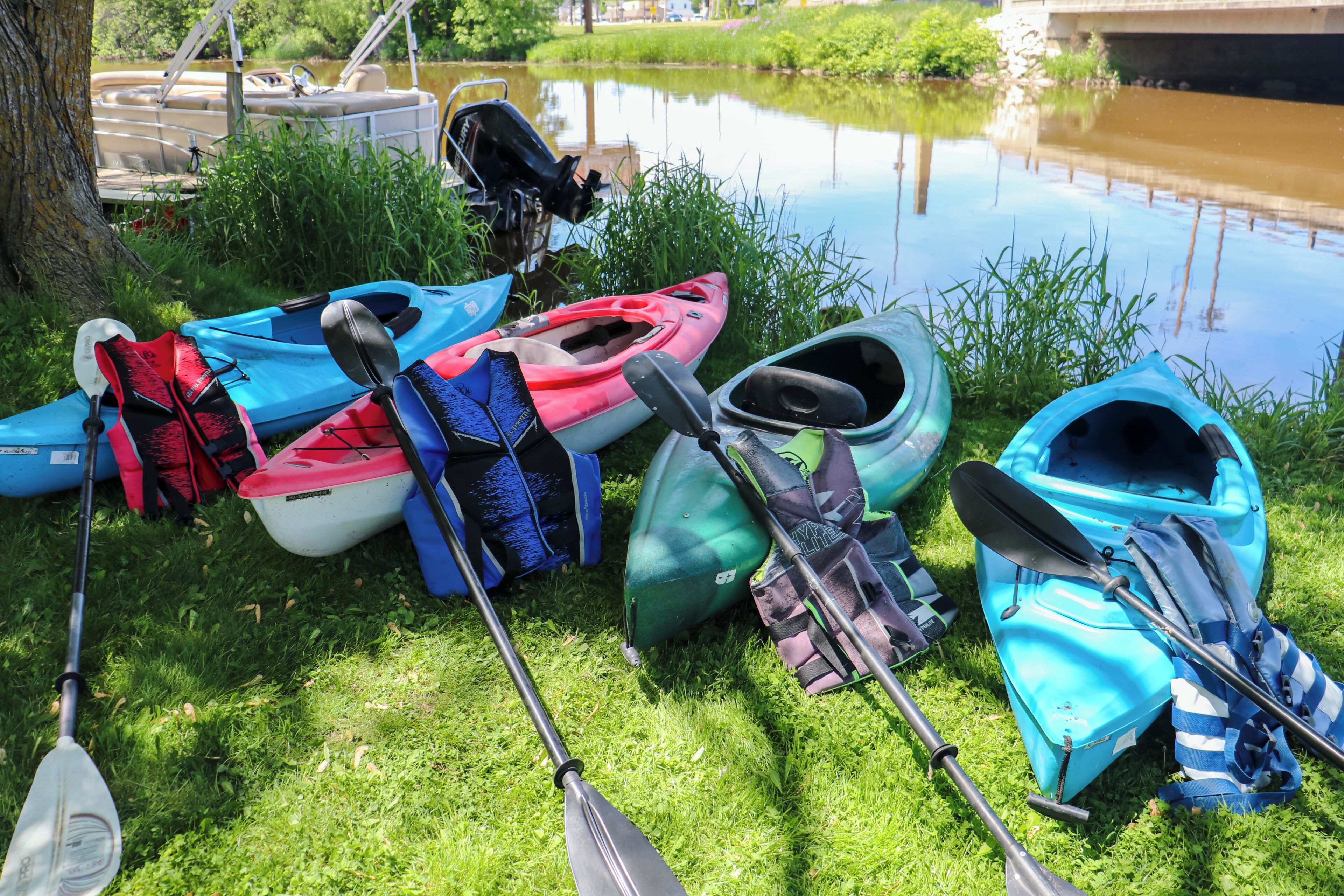 Des kayaks et des pagaies sont posés sur l’herbe, près d’une étendue d’eau calme.