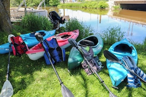 Kayaks y palas sobre césped cerca de un cuerpo de agua tranquilo.