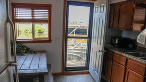 Uma cozinha compacta com armários de madeira, micro-ondas embutido e porta de vidro deslizante para uma varanda.