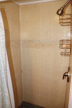 A shower area with beige tiles, a metal shower head, and a towel rack.