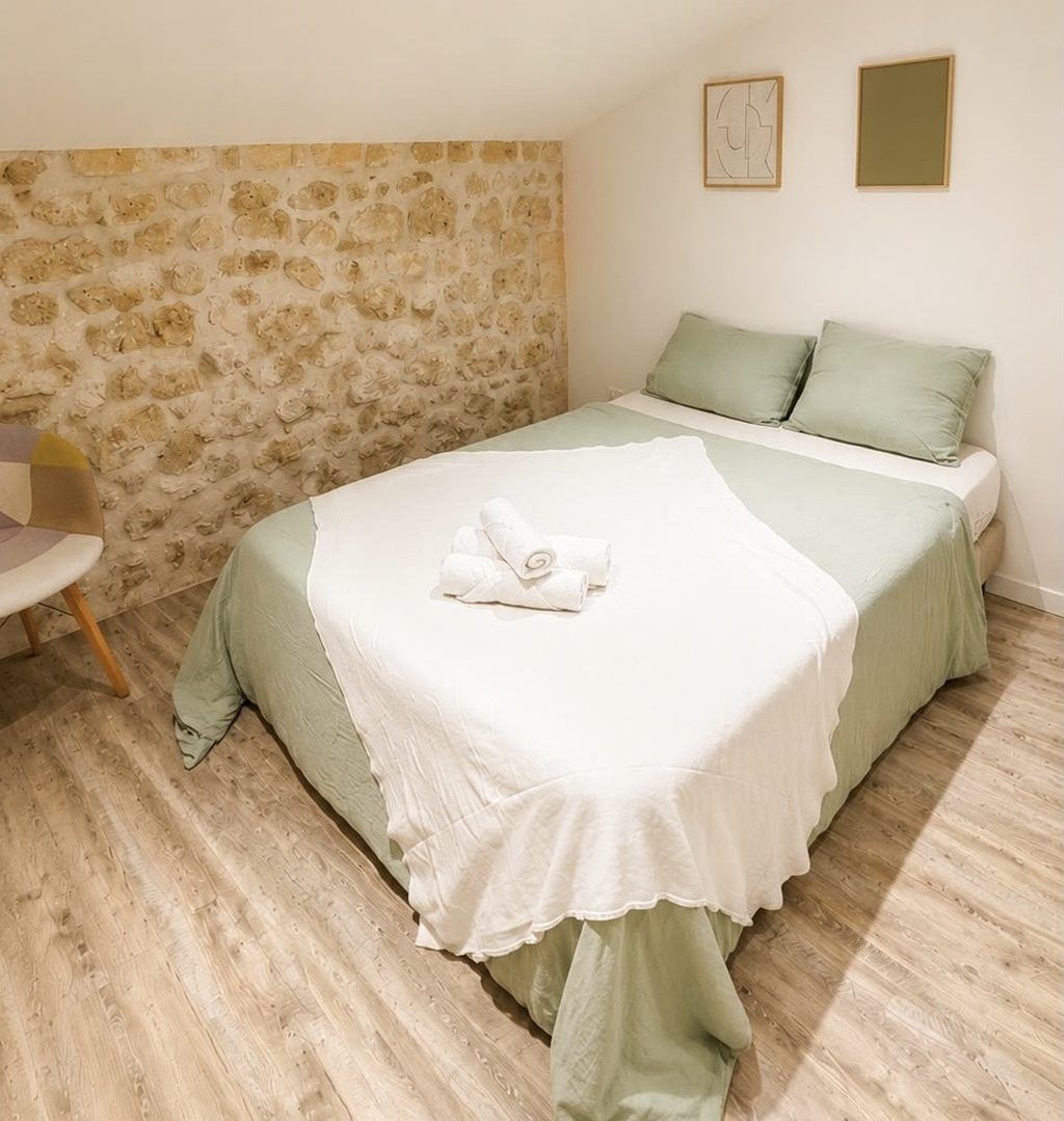 Een slaapkamer met een stenen muur, een bed met groen beddengoed en een stoel.