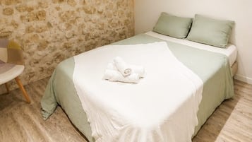 Een slaapkamer met een stenen muur, een bed met groen beddengoed en een stoel.