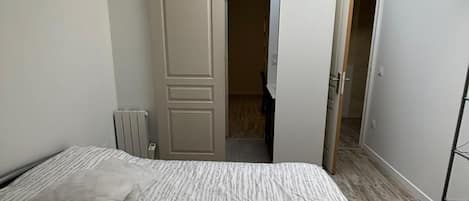 A bedroom with a bed, a radiator, a wardrobe, and a door leading to another room.
