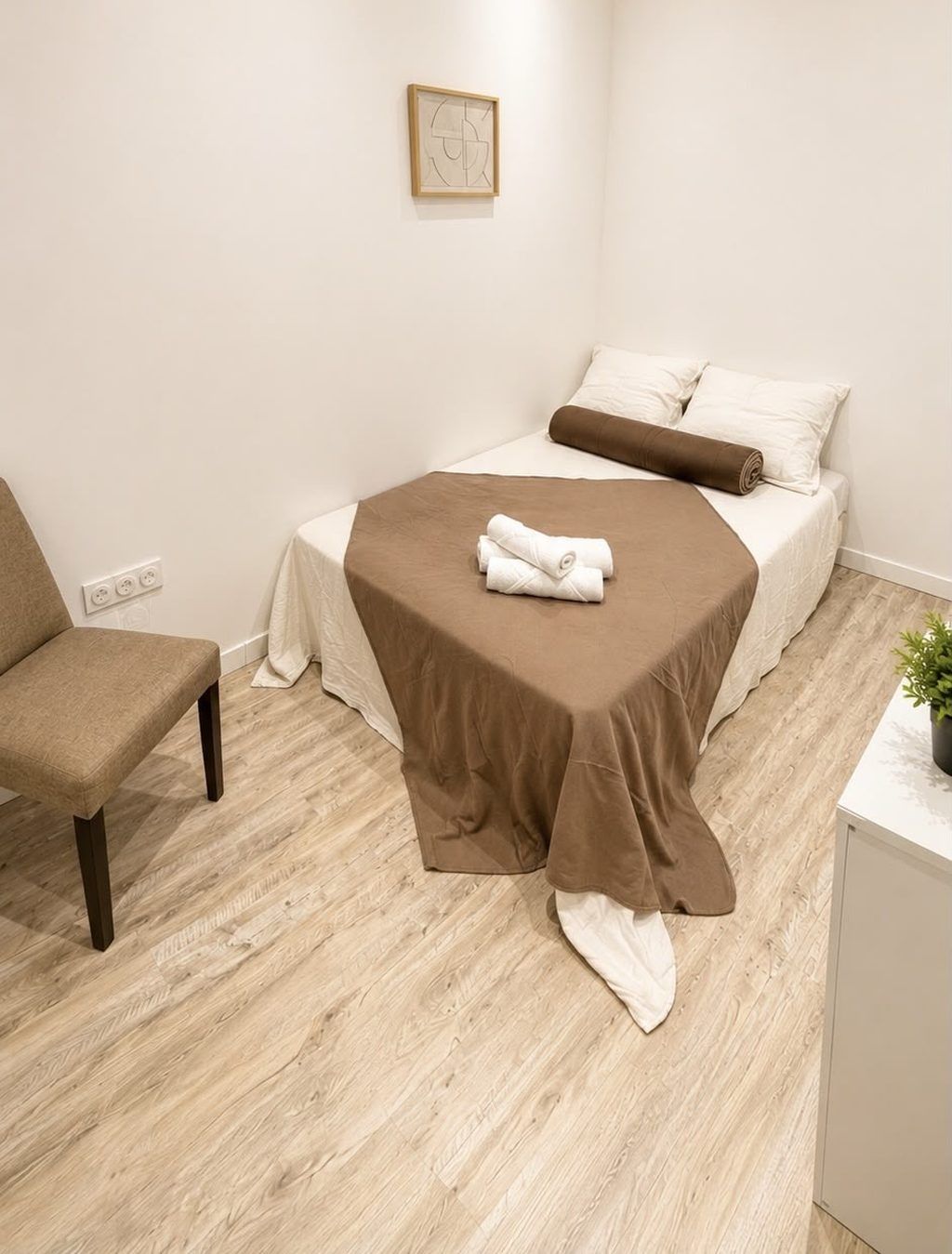 A small, neatly arranged room with a single bed, a chair, and a small table.