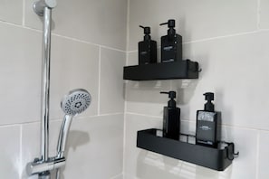 Ein Badezimmer mit Dusche, zwei schwarzen Ablagen für Pflegeprodukte und einem chromfarbenen Duschkopf.