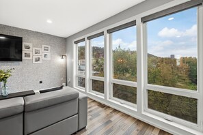 Un salon moderne doté d’une grande fenêtre, d’un téléviseur à écran plat et d’un mur orné d’un motif décoratif.
