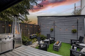 Patio trasero con una parrilla, mobiliario exterior y una fogata.