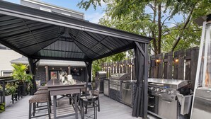 An outdoor kitchen with a covered dining area, bar stools, and a grill. - Hot tub, BBQ, Fire pit, Garage, Near Downtown (Pittsburgh)