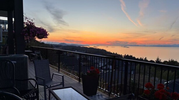 Ein Balkon mit Gartenmöbeln, einem Geländer und Blick auf den Sonnenuntergang über dem Wasser.