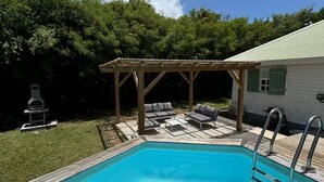 A swimming pool with a wooden deck, a covered seating area, and a house in the background. - Kaz'Ary Entire villa in Sainte-Anne, Guadeloupe (Sainte‑Anne)
