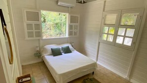 A bedroom with a bed, a window, a radiator, and a small table with a plant. - Kaz'Ary Entire villa in Sainte-Anne, Guadeloupe (Sainte‑Anne)