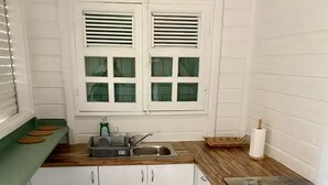 A compact kitchen with a sink, a washing machine, and a window with blinds. - Kaz'Ary Entire villa in Sainte-Anne, Guadeloupe (Sainte‑Anne)