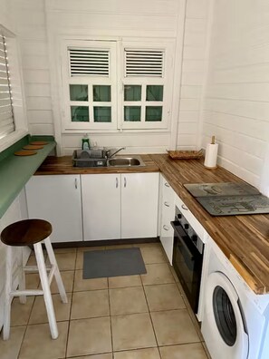 A compact kitchen with a sink, a washing machine, and a window with blinds. - Kaz'Ary Entire villa in Sainte-Anne, Guadeloupe (Sainte‑Anne)