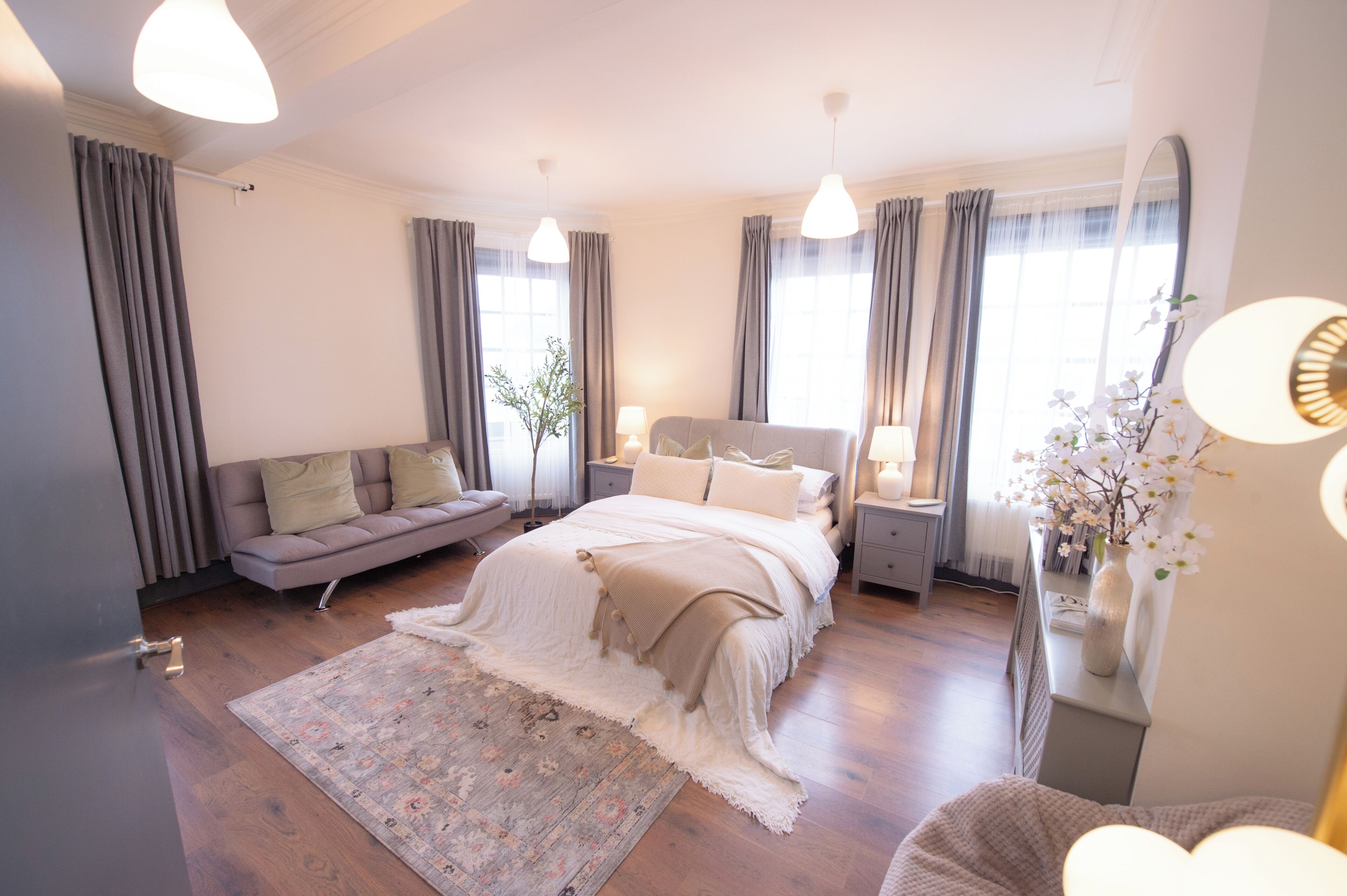 A bedroom with a bed, a sofa, a nightstand, a mirror, and a window.