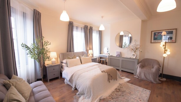 Un dormitorio con cama, mesitas de noche, escritorio, silla, espejo y lámpara.