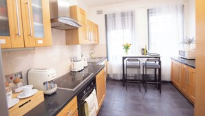 Una cocina moderna con armarios de madera, encimera negra, horno integrado, cafetera y comedor con dos sillas y una mesa.
