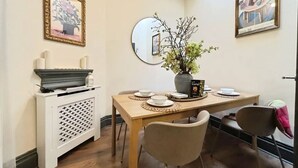 Un comedor con una mesa de madera, dos sillas, un florero con flores, un espejo y obras de arte enmarcadas en las paredes.