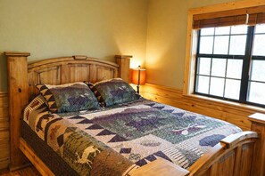 Un lit en bois avec une courtepointe, une lampe de chevet et une fenêtre avec des stores.