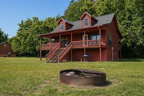 A red wooden house with a porch, a fire pit, and a grill in the yard.