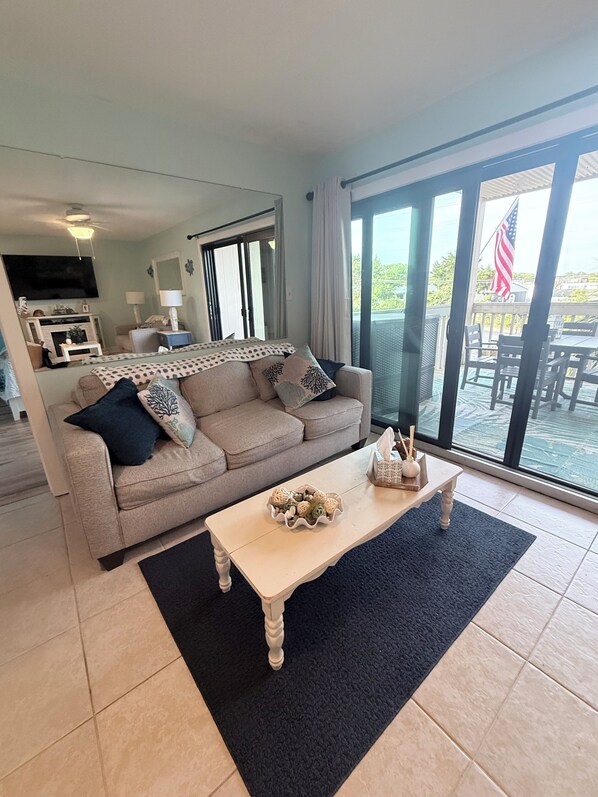 A living room with a beige sofa, a coffee table, and a large sliding glass door leading to an outdoor patio. - Wonderful 2-bedroom condo with AC and 2 pools in Myrtle Beach (Myrtle Beach)
