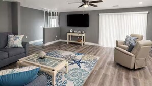 Ein Wohnzimmer mit Sofa, Sessel, Couchtisch und einem an der Wand befestigten Fernseher.